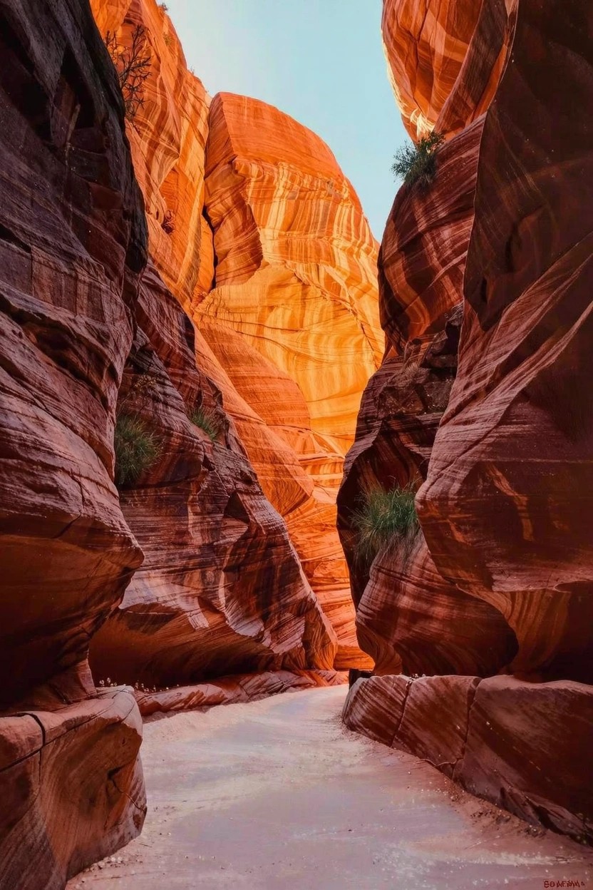 Painting of a slot canyon with towering curved red rock walls, sandy path in the center, sparse green plants, and blue sky above.