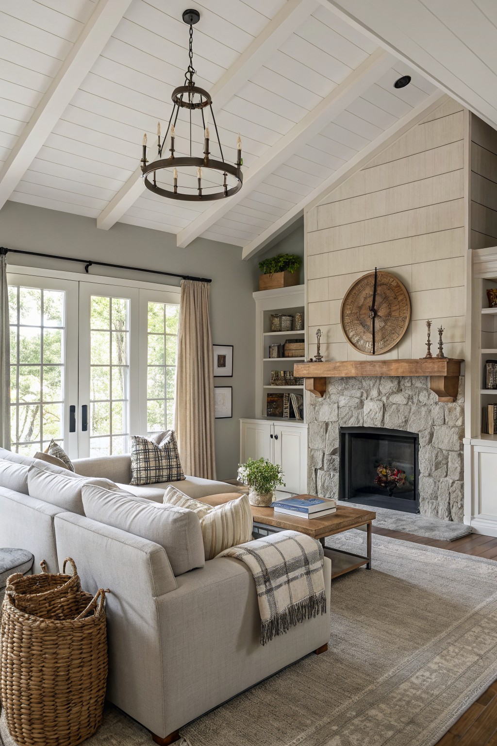 Living room with light greige walls, vaulted white shiplap ceiling, stone fireplace with wood mantel, neutral sofa, and large windows with cream drapes