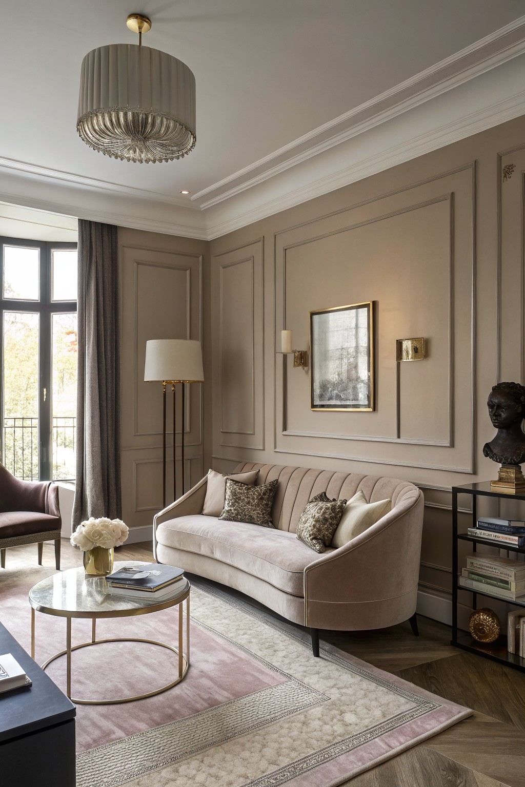 Living room with soft greige paneled walls, blush pink velvet curved sofa, glass coffee table, tall floor lamp, and window overlooking trees