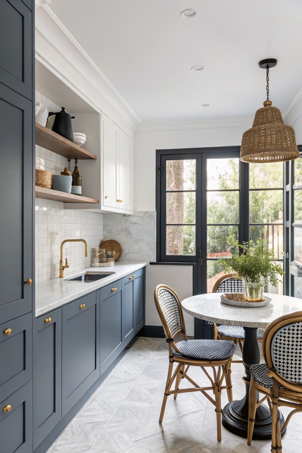 Kitchen featuring deep navy lower cabinets with white uppers, marble counters, gold faucet, and round table with bistro chairs