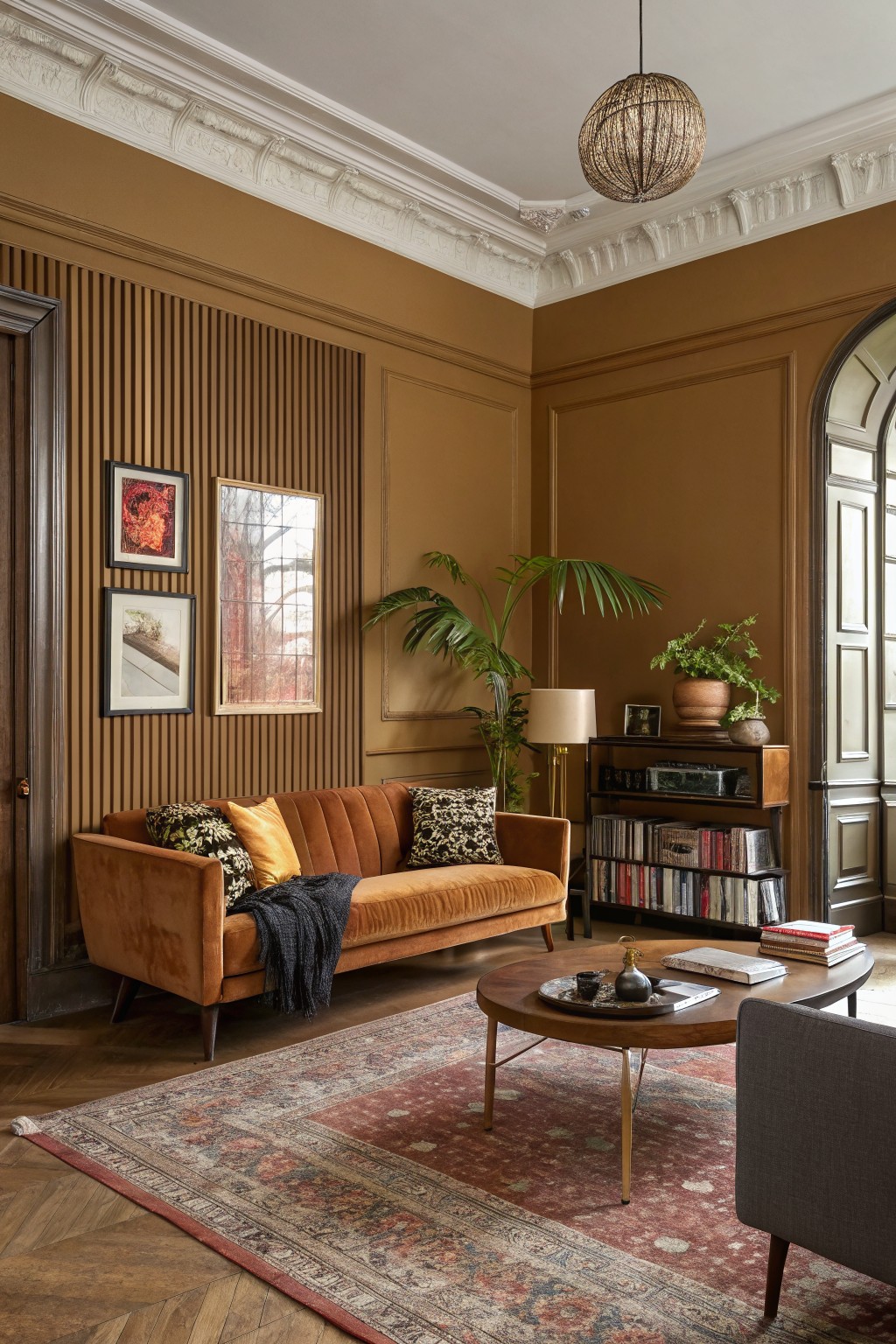 Living room corner with warm terracotta walls, orange velvet sofa, slatted wood paneling, plants, and wood floors