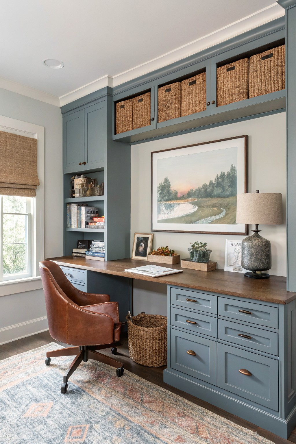 Cozy home office featuring deep navy blue cabinets with wood desktop, leather desk chair, seagrass baskets, and soft gray walls