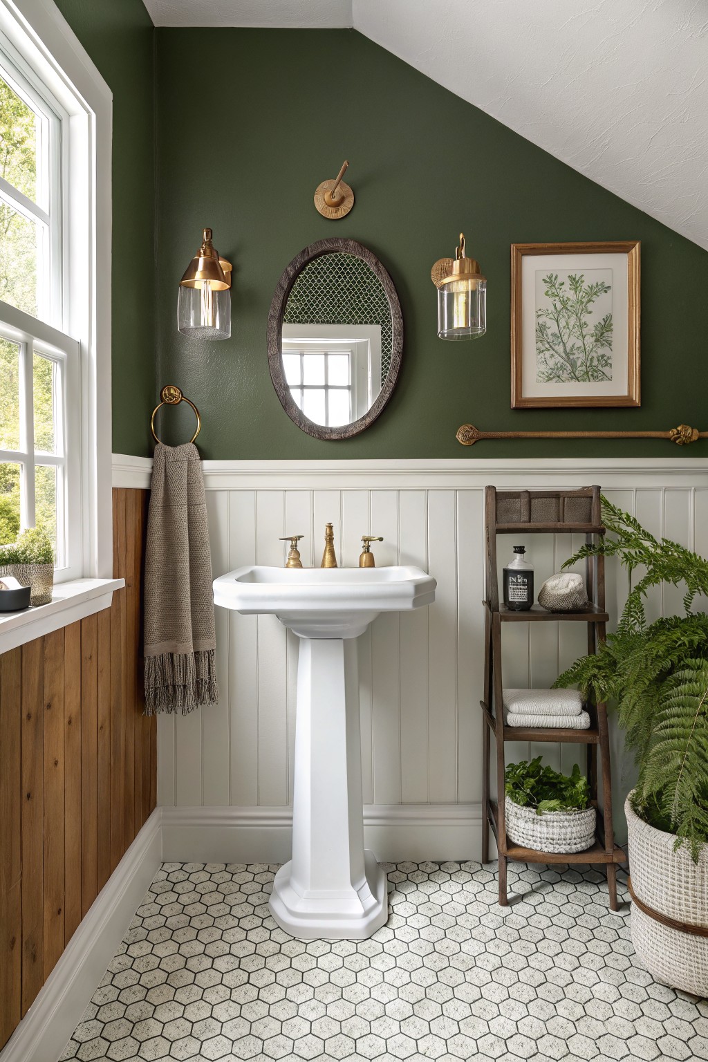 Sage green upper walls in a bathroom with white wainscoting, wood paneling, pedestal sink, brass accents, and potted plants on hexagonal tile floor