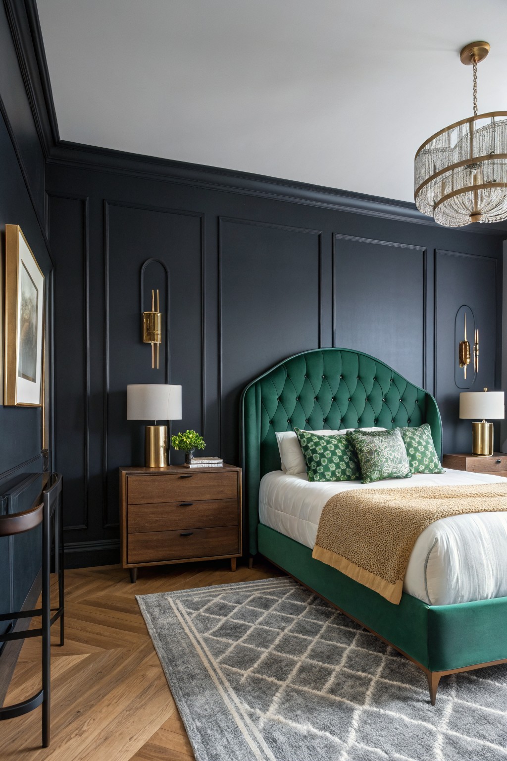 Bedroom interior with deep navy paneled walls, emerald velvet bed, gold sconces and chandelier, wood nightstand, and herringbone rug