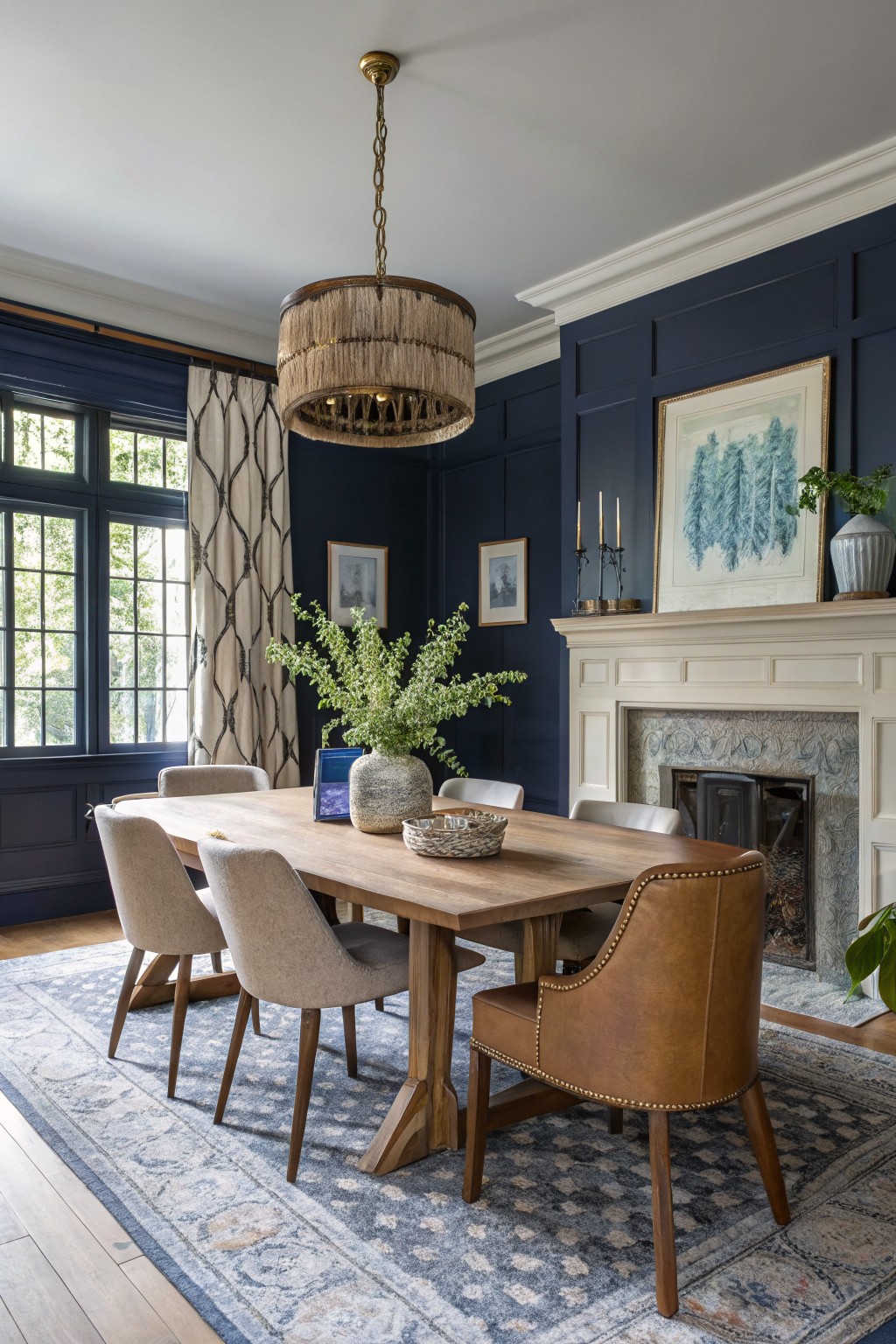 Cozy dining room with deep navy paneled walls, wooden table, leather chairs, fireplace, and rattan chandelier