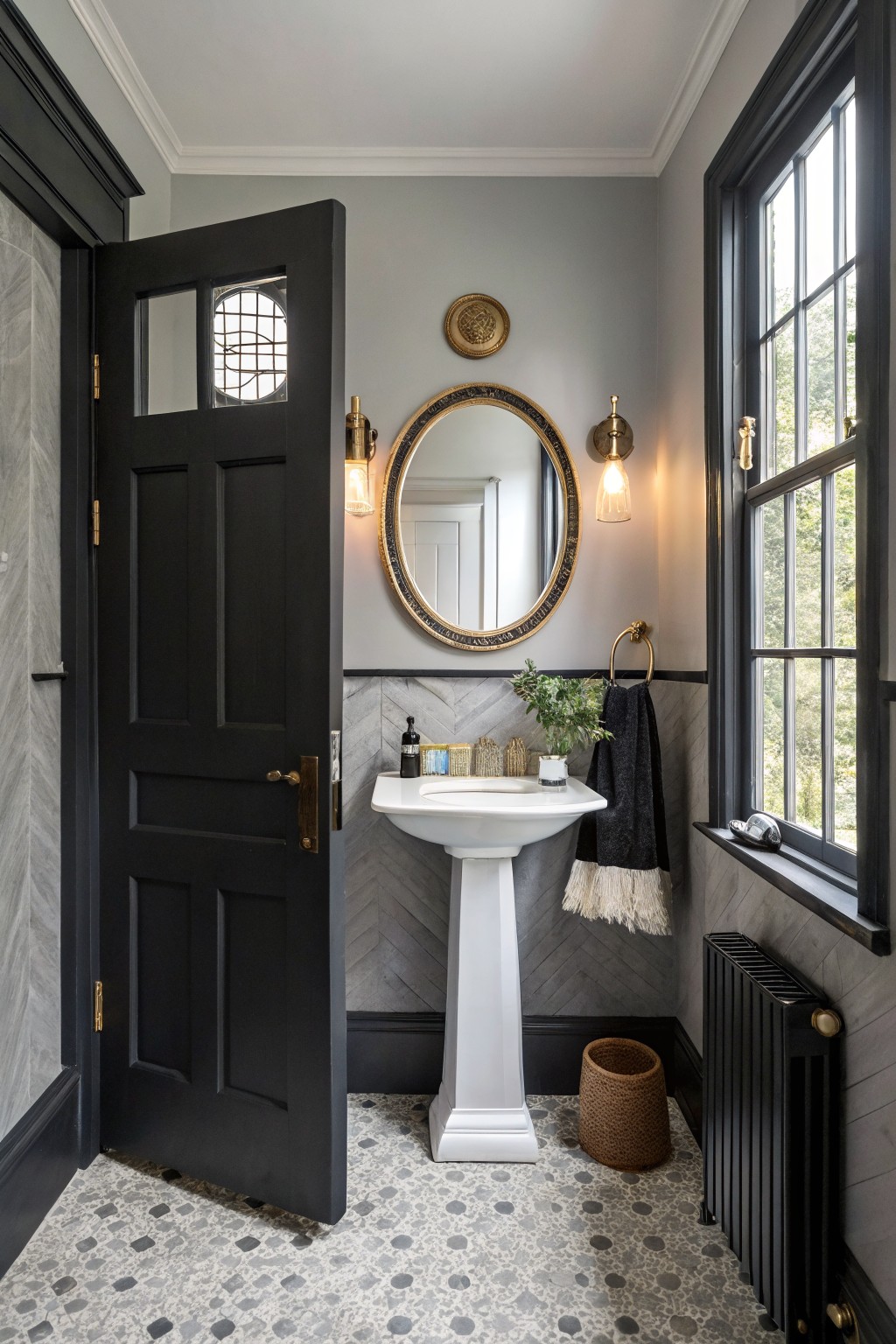 Powder room featuring soft cool gray walls accented by black trim, a white pedestal sink, and herringbone gray tile backsplash
