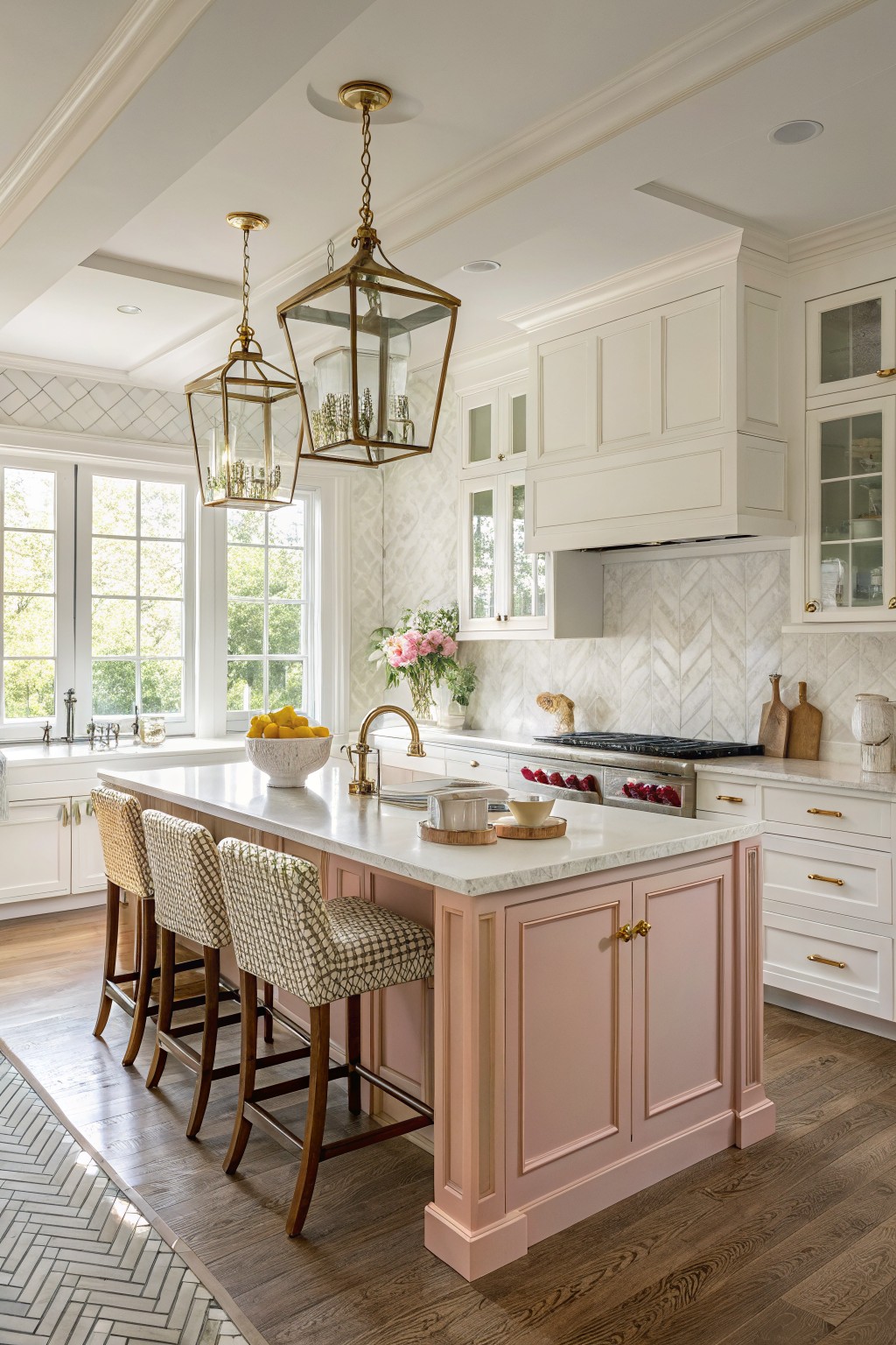 Bright kitchen with white cabinets, a pink island, gold hardware, and herringbone floors