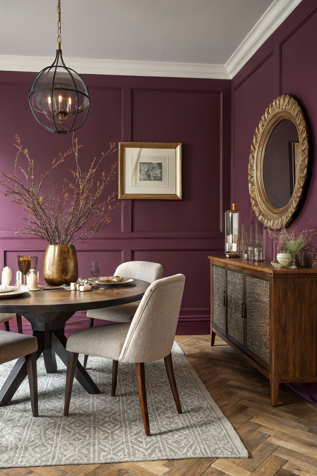 Dining room with warm plum purple paneled walls, oval wood table, cream chairs, gold mirror and brass accents on hardwood floors
