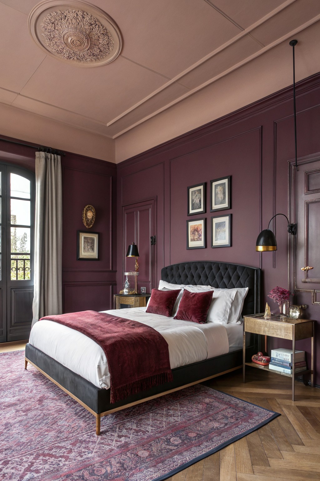 Bedroom with deep maroon paneled walls, black velvet bed, brass accents, and Persian rug on herringbone floors