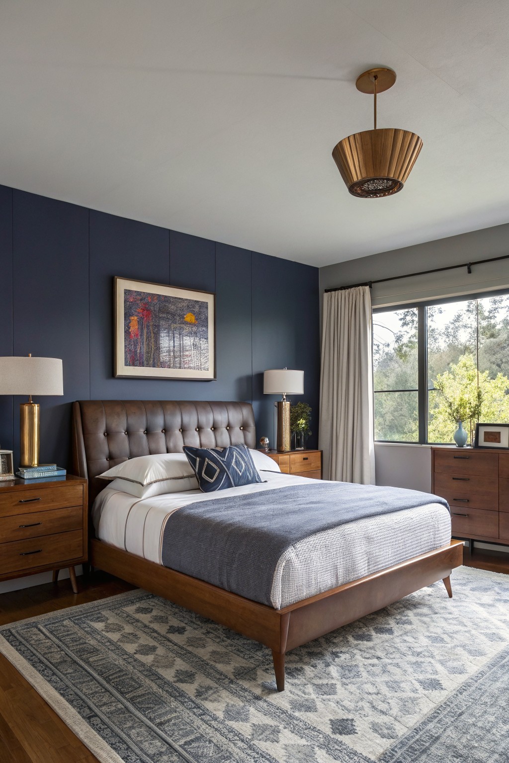 Cozy bedroom featuring a deep navy paneled accent wall behind a leather-upholstered wood bed frame, flanked by matching nightstands and brass lamps, with a large window showing greenery outside