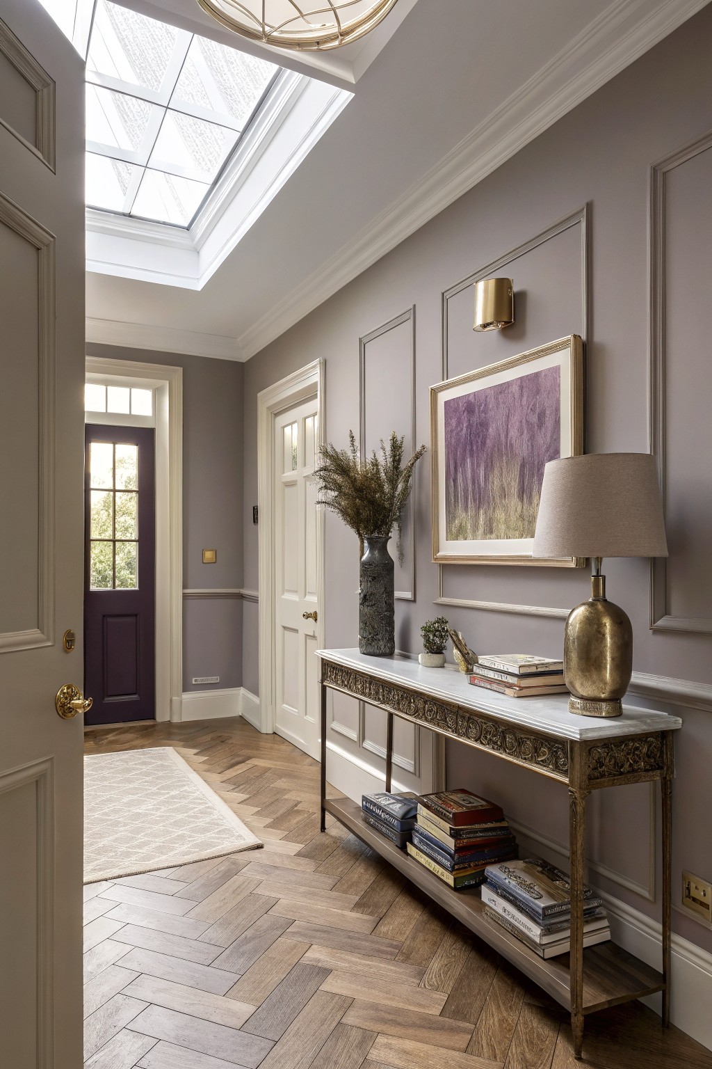 Hallway interior with soft greige paneled walls, ornate gilded console table holding books and lamp, herringbone wood floors, and front door visible
