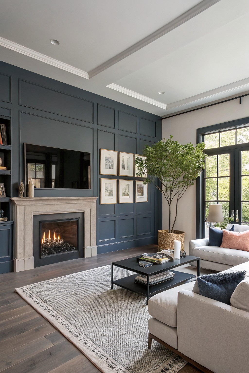 Cozy living room featuring deep navy blue paneled walls, cream sectional sofa, stone gas fireplace, and potted tree by black-framed windows