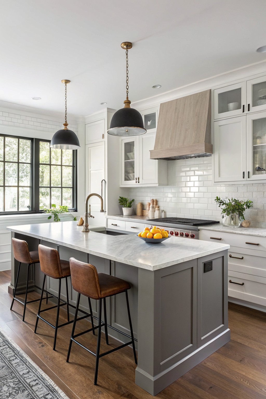 Modern kitchen with gray island cabinets, white upper cabinets, marble counters, and wood floors under black pendant lights