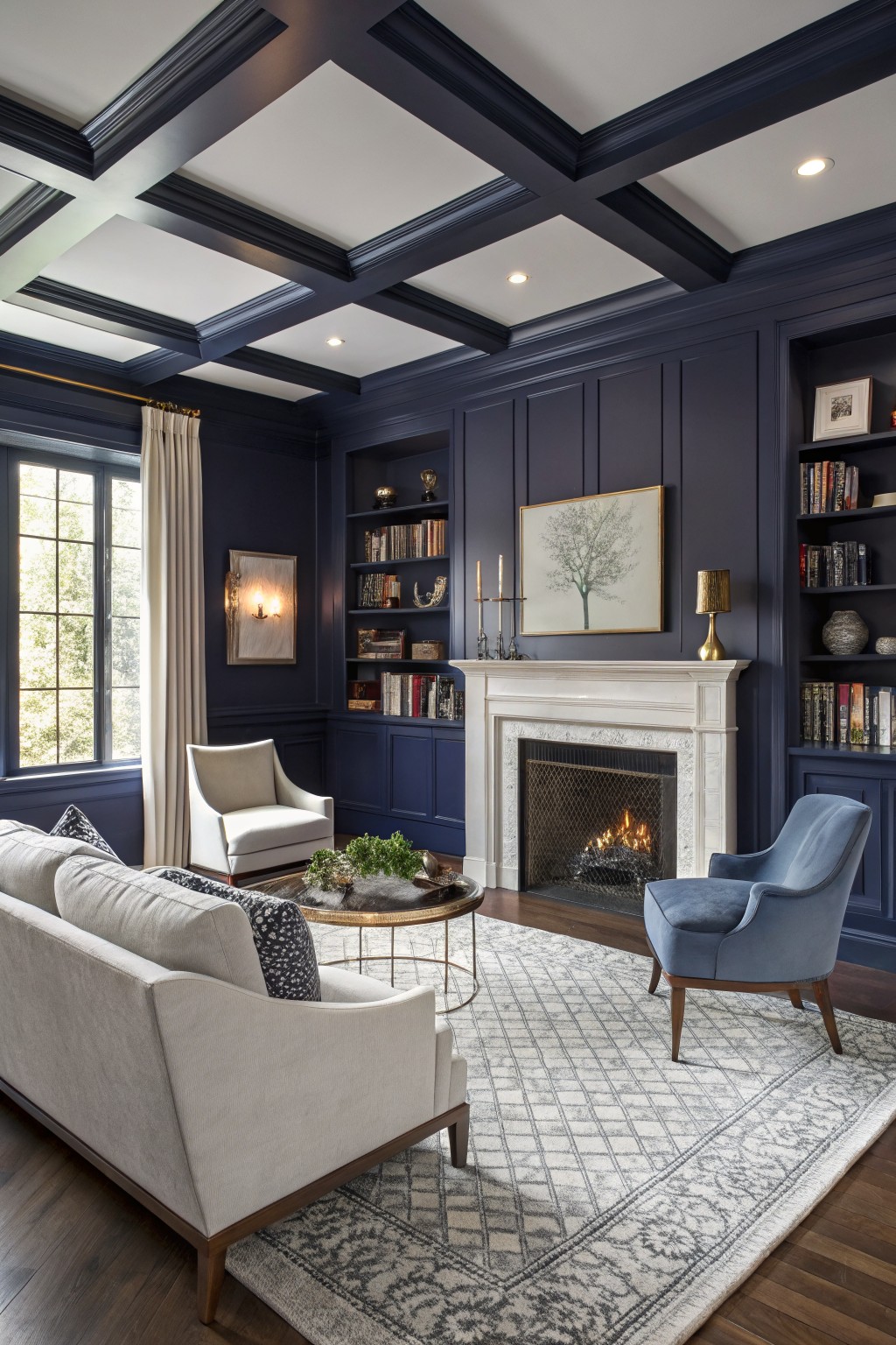 Living room with deep navy paneled walls and beamed ceiling, cream sofa and chairs, marble fireplace, bookshelves, and hardwood floors