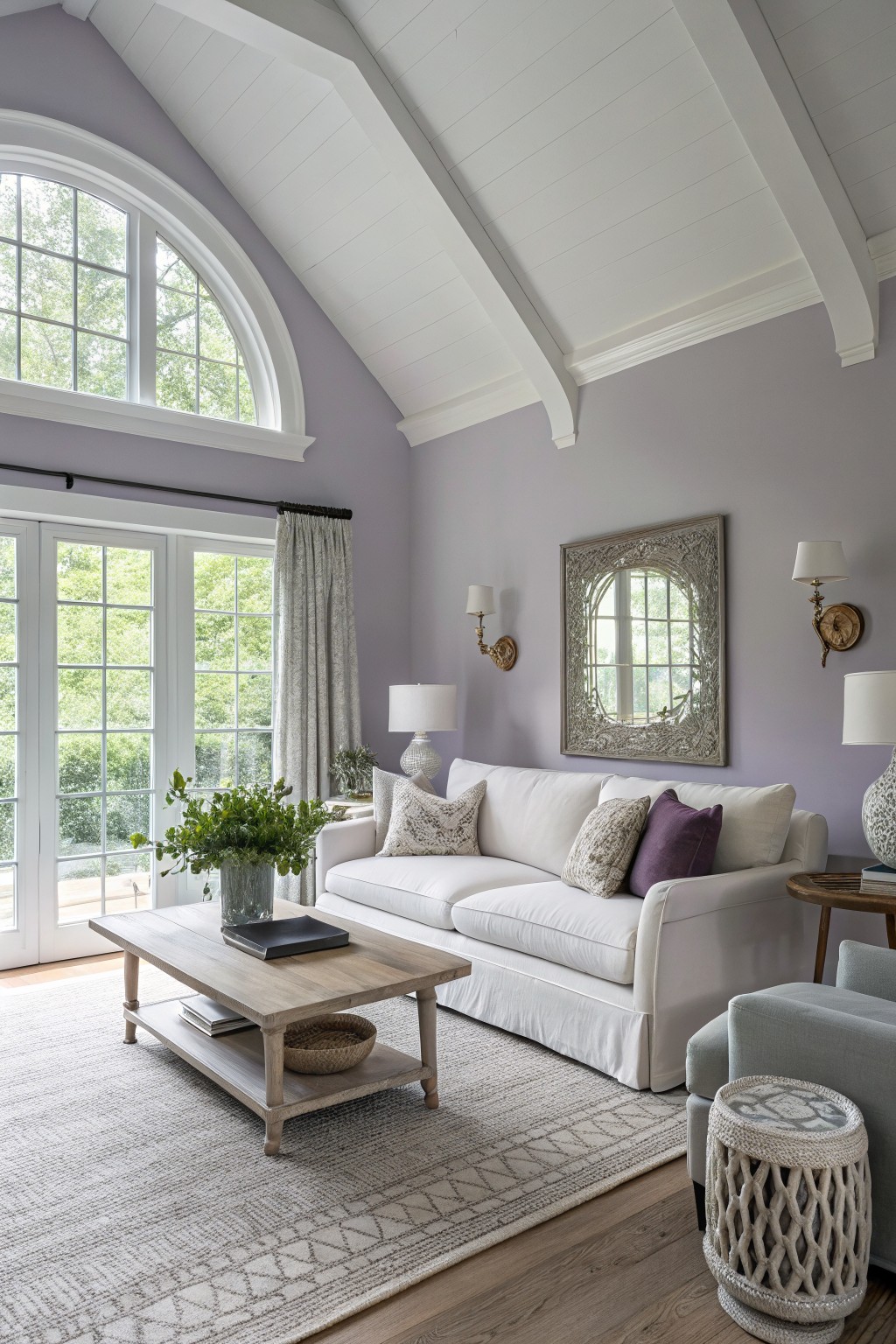 Cozy living room featuring pale lavender walls, white beamed ceiling, plush sofa, and large windows with views of greenery