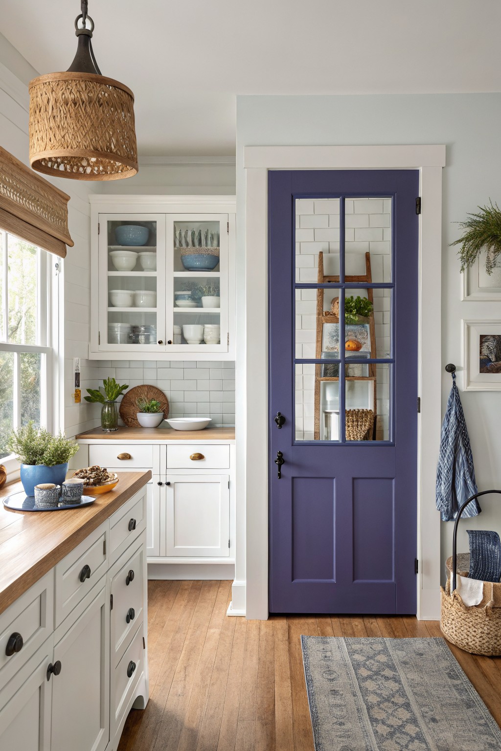 Cozy kitchen corner with white cabinets, wood counters, subway tile, plants, and a bold purple glass door framed in white.