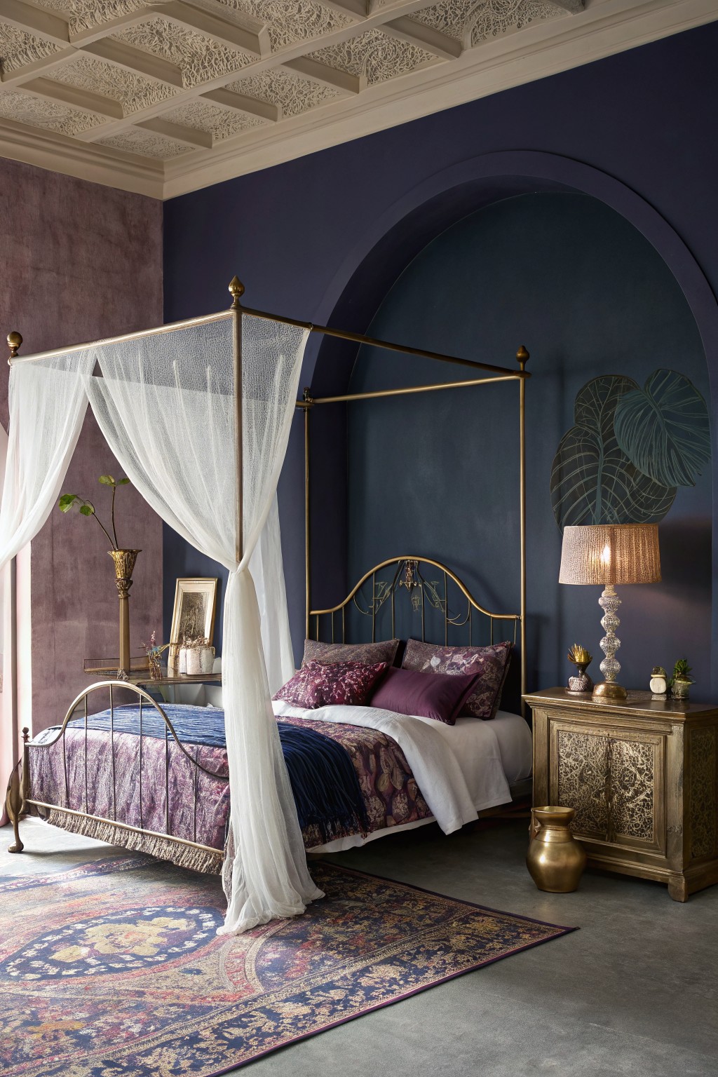 Bedroom featuring deep navy walls with arched accent, gold four-poster canopy bed draped in white sheers, plush purple bedding, ornate gold furniture, and Persian-style rug