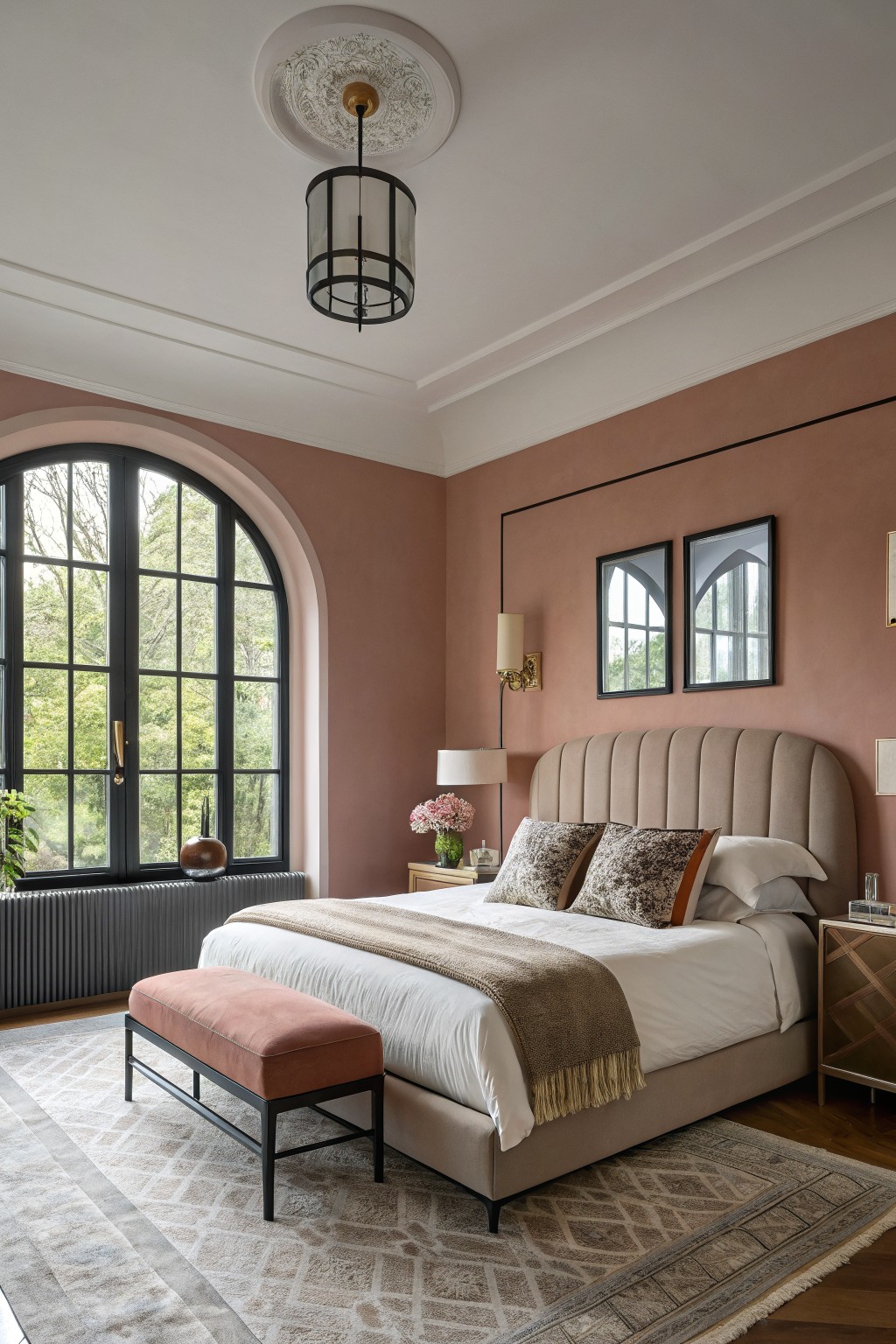 Bedroom interior with warm blush pink walls, tufted beige bed, arched black window, and wooden floors