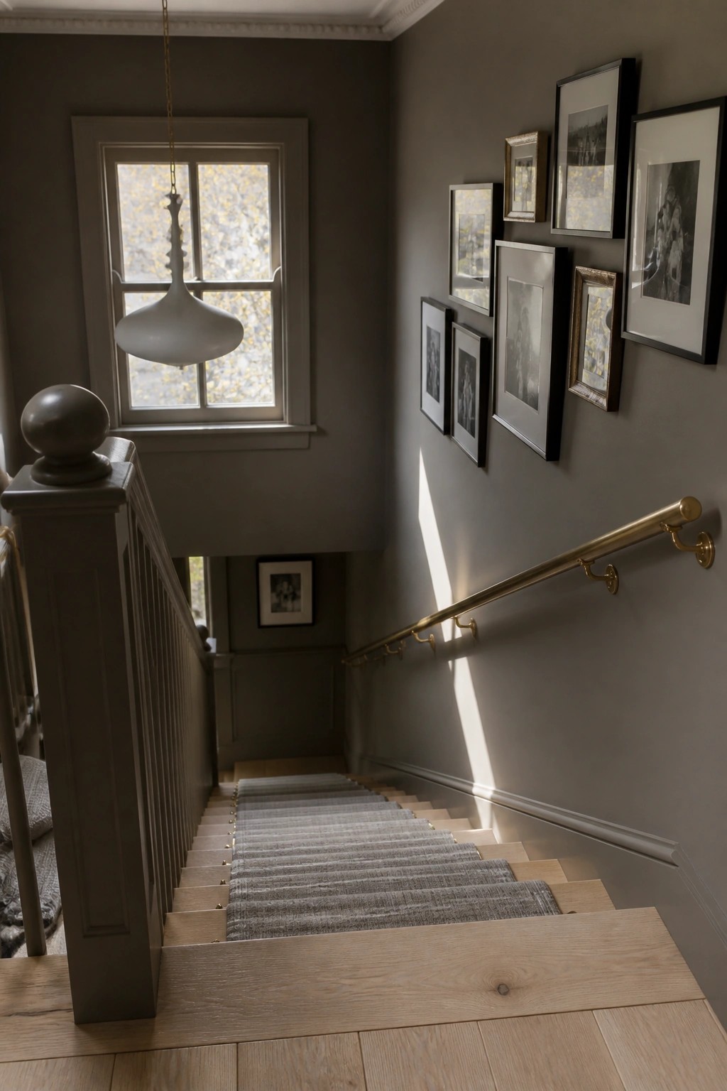 Gray staircase with wooden steps, gray runner, brass handrail, framed gallery wall, and pendant light