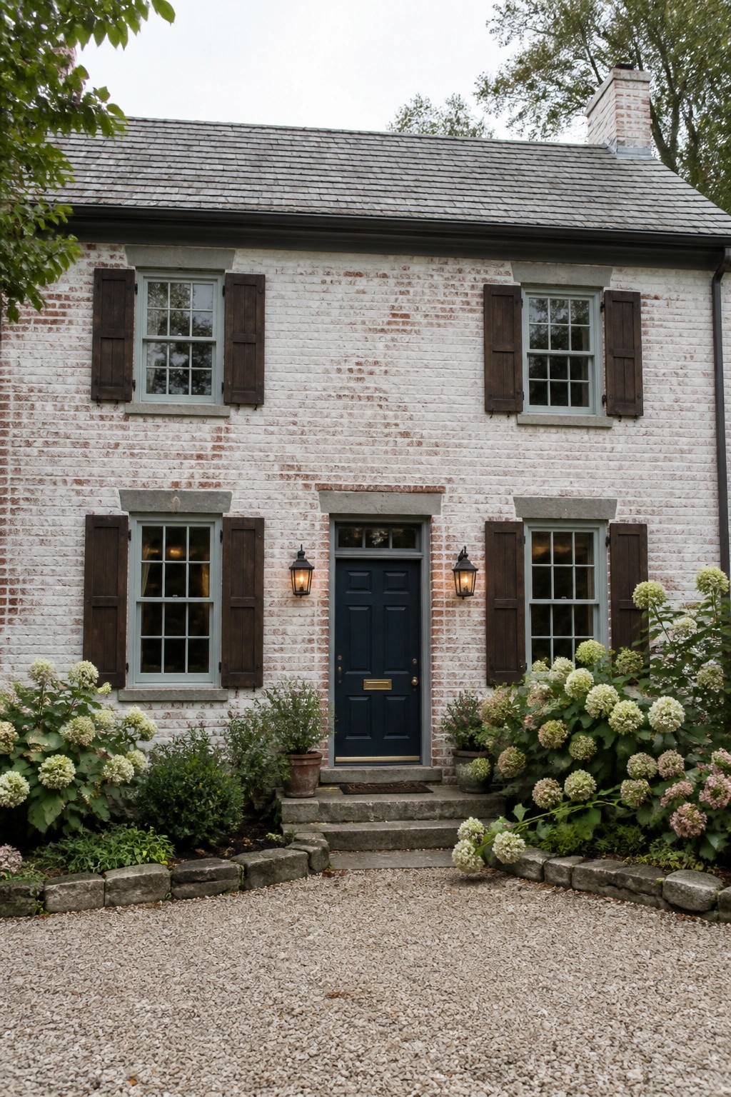 White brick house with dark blue door, brown shutters, and blooming hydrangeas.