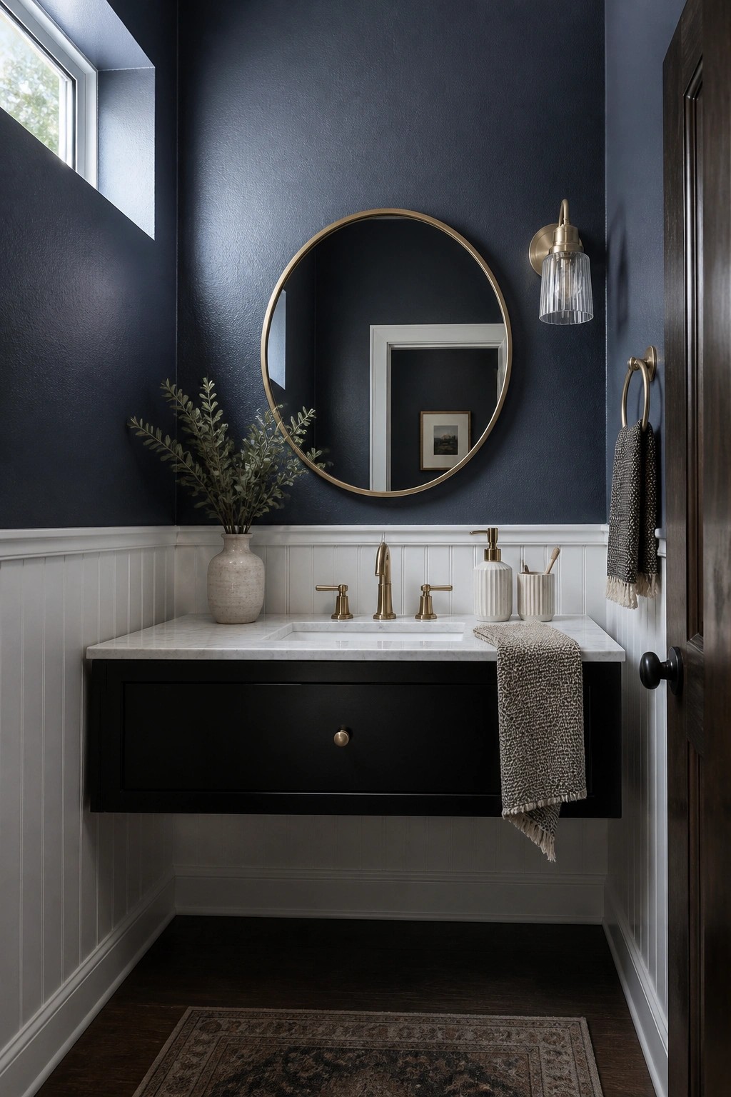Modern bathroom with navy walls, floating black vanity, round gold mirror, and brass fixtures.