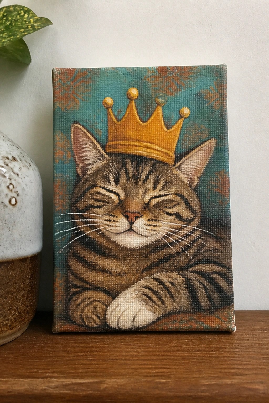 Close-up painting of a tabby cat wearing a golden crown, eyes closed on teal.