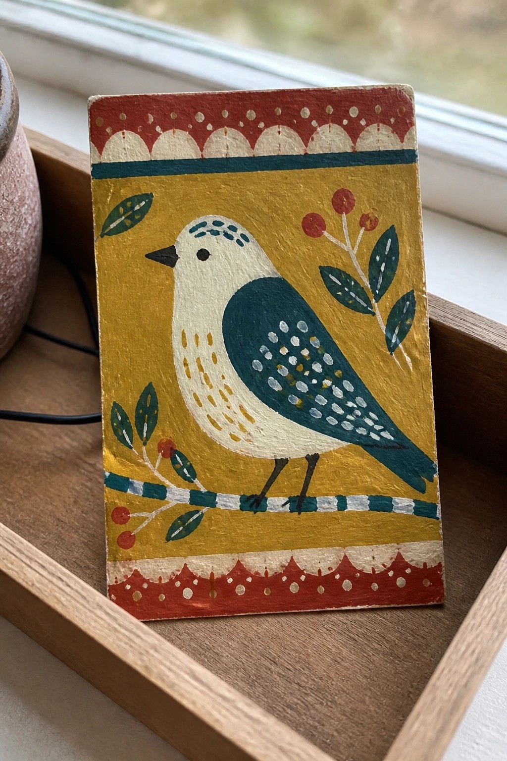 Folk art painting of teal bird on branch with red scalloped borders on yellow background