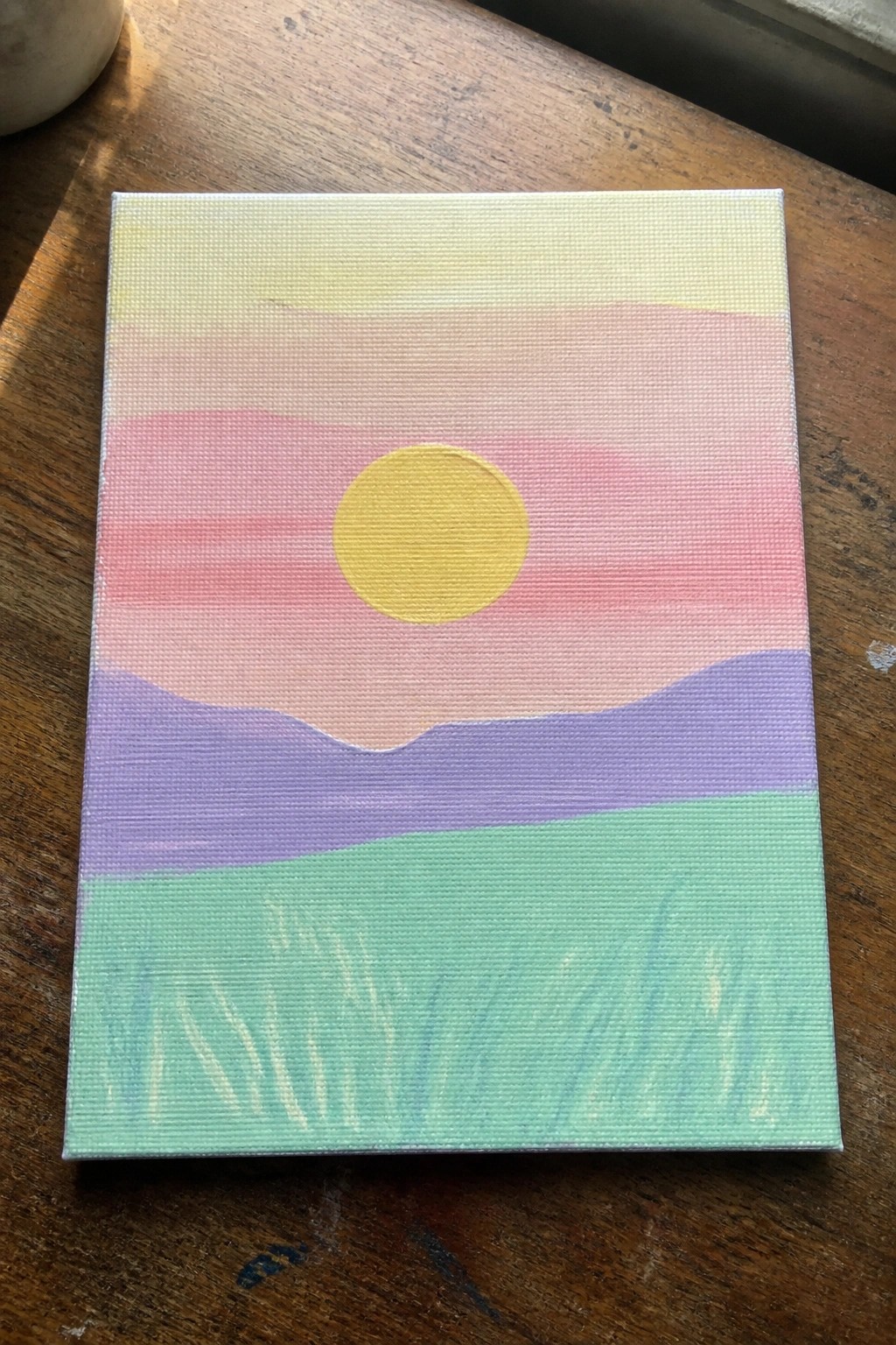 Vibrant sunset painting with yellow sun over layered pink, purple, and green hills.