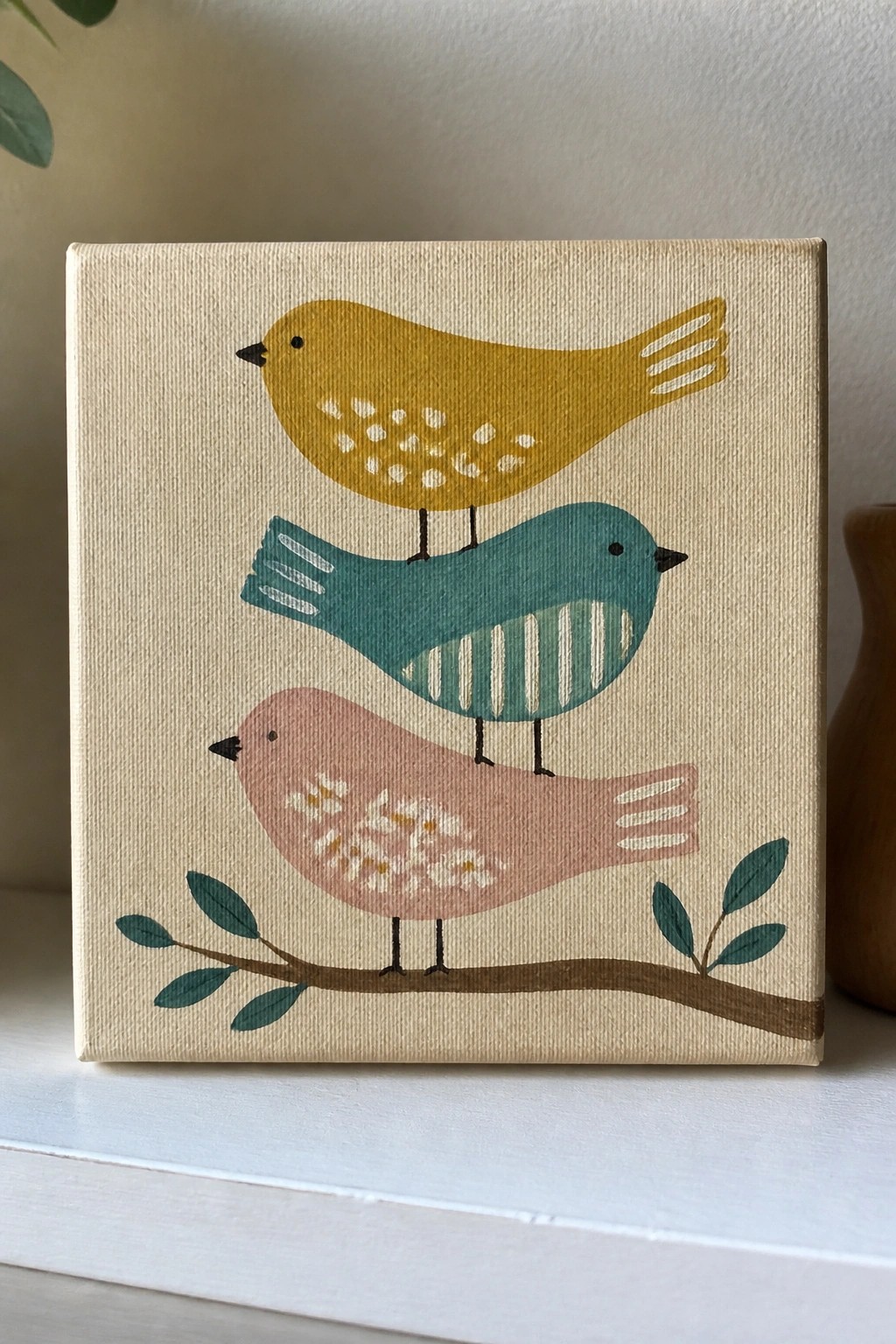 Three birds in yellow, teal, and pink perched on a branch with green leaves