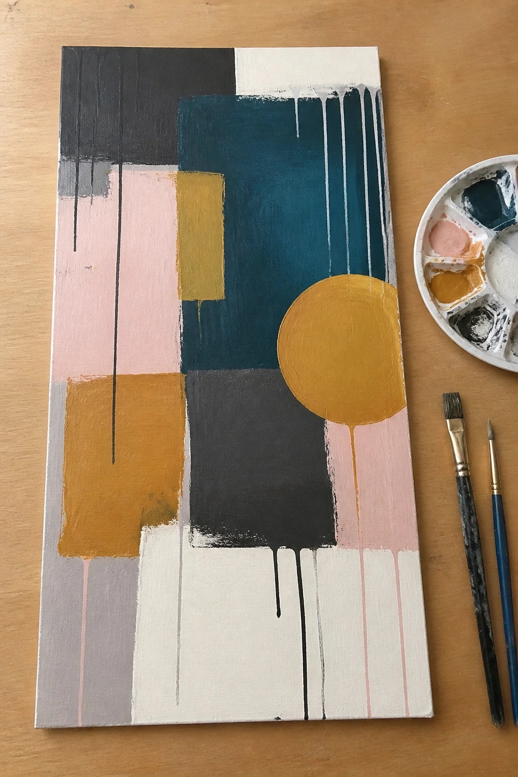 Abstract geometric painting with teal, pink, yellow shapes and drips beside palette and brushes.