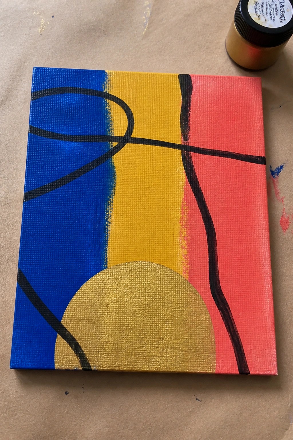 Abstract painting with blue yellow pink sections, black curves, gold semicircle beside paint bottle.
