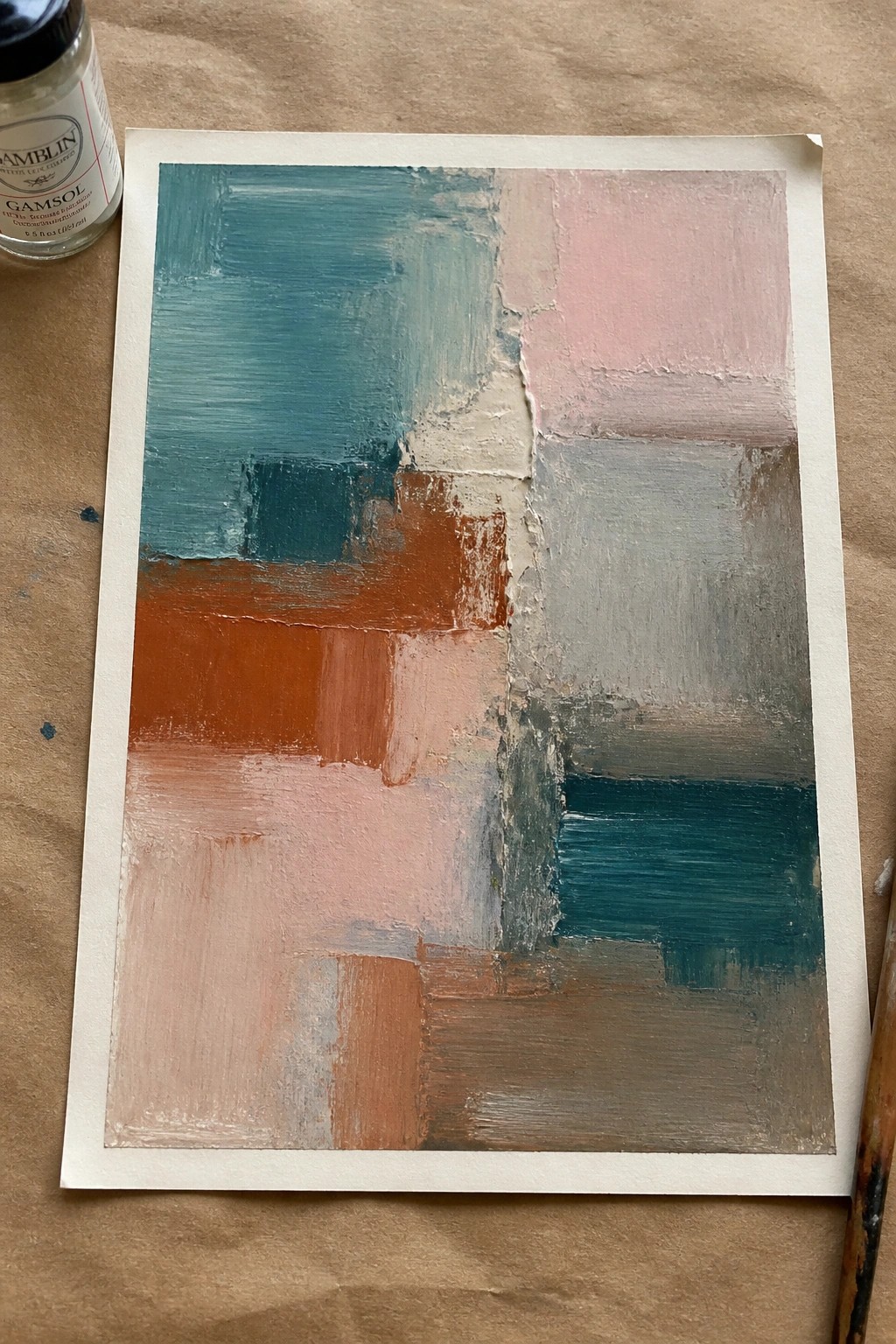 An abstract oil painting of rectangular blocks in teal, orange, pink, gray, and brown tones on white paper, next to a bottle of Gamsol.