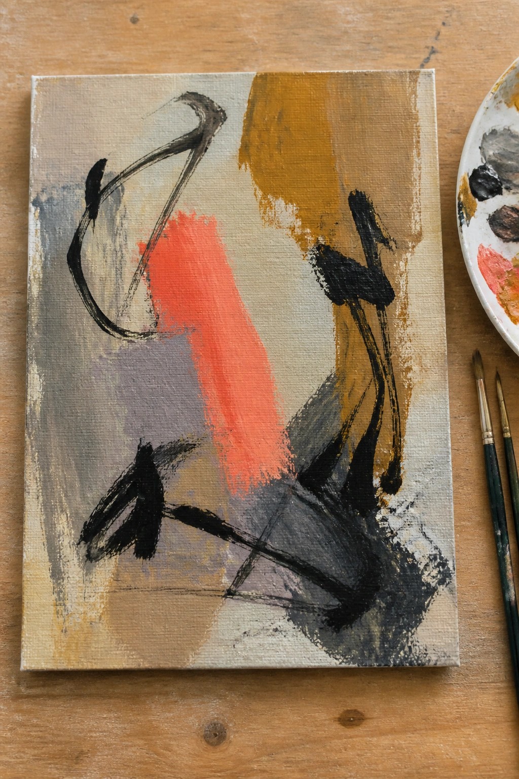 Abstract painting with black strokes, red shape, and brown tones beside palette and brushes