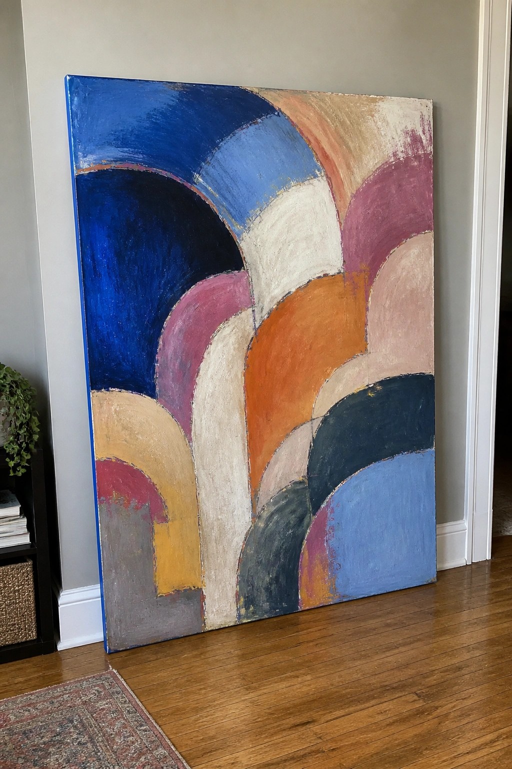 Large abstract painting with colorful curved arches leaning against wall on wooden floor.