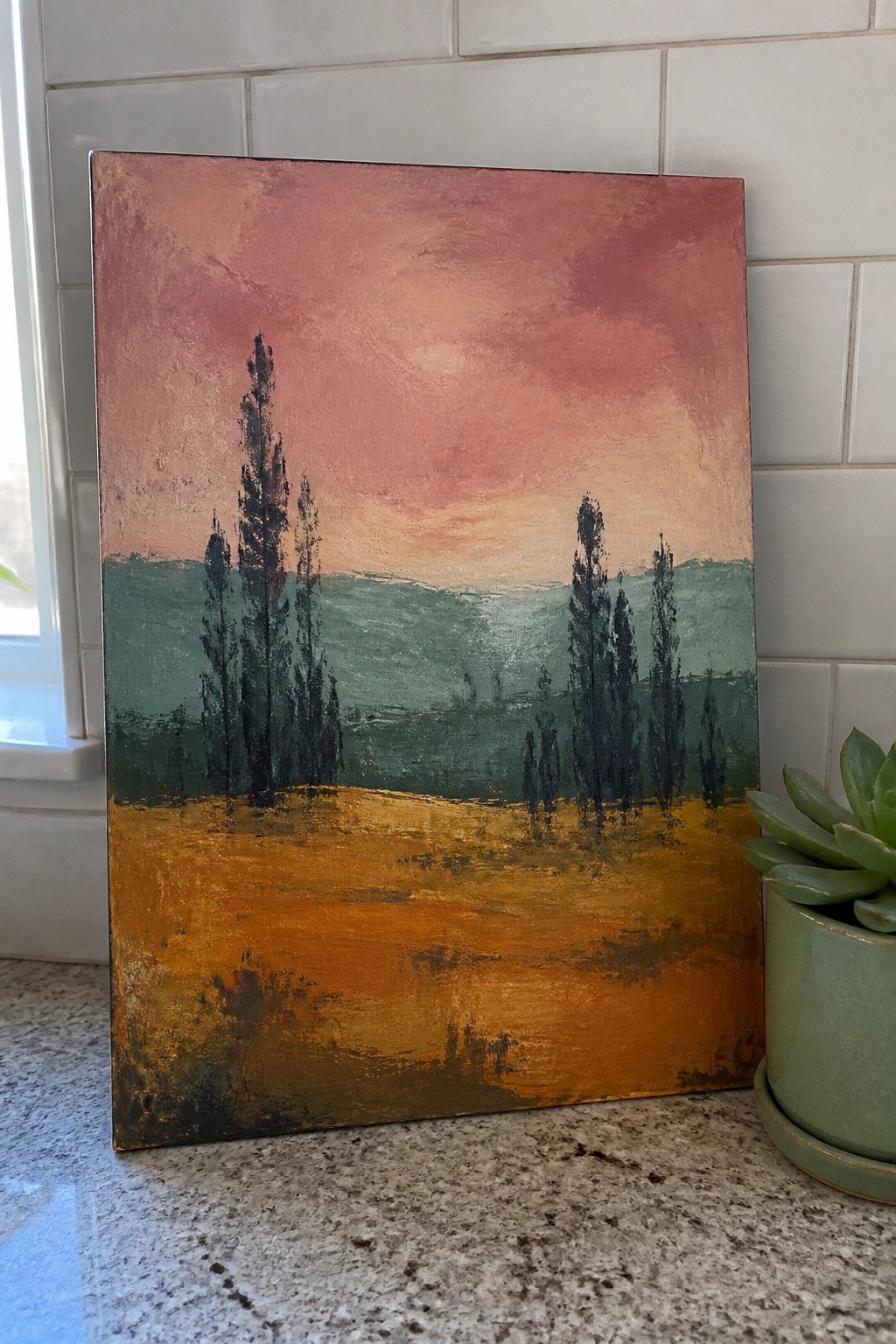 Abstract landscape painting with pink sky, green hills, dark trees, and golden field beside succulent.