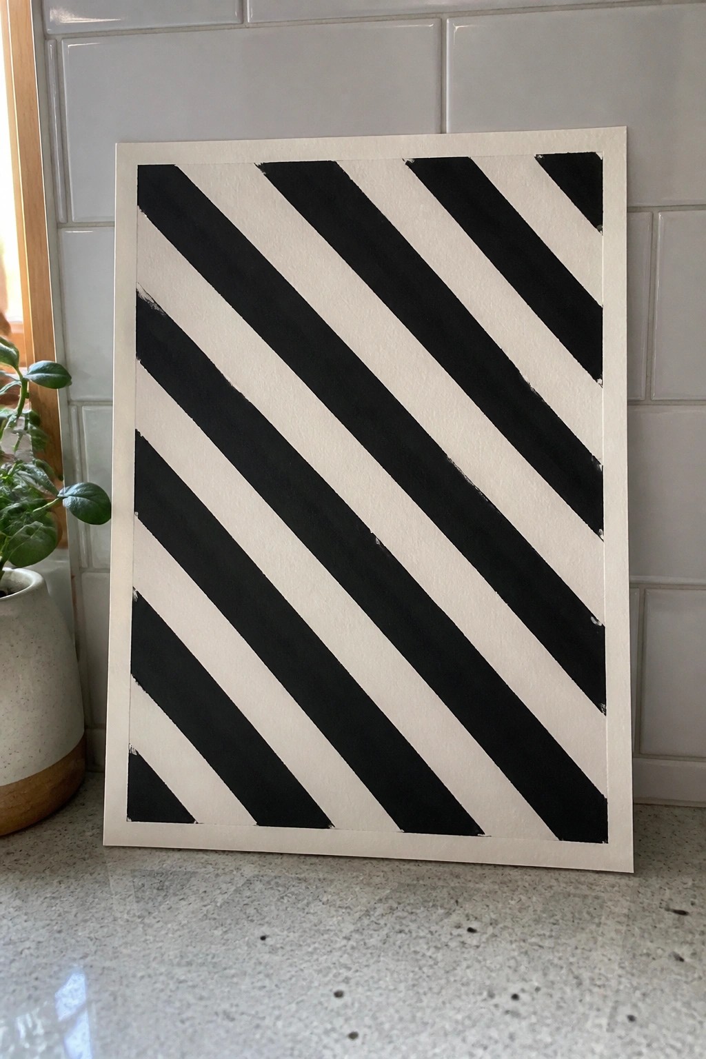 Black and white diagonal striped artwork on counter beside potted plant and tiles.
