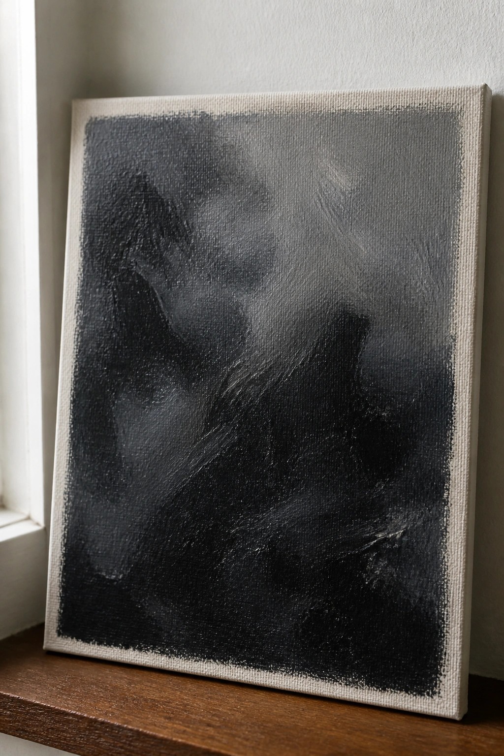 Abstract black-and-gray textured painting on canvas resting on wooden ledge.