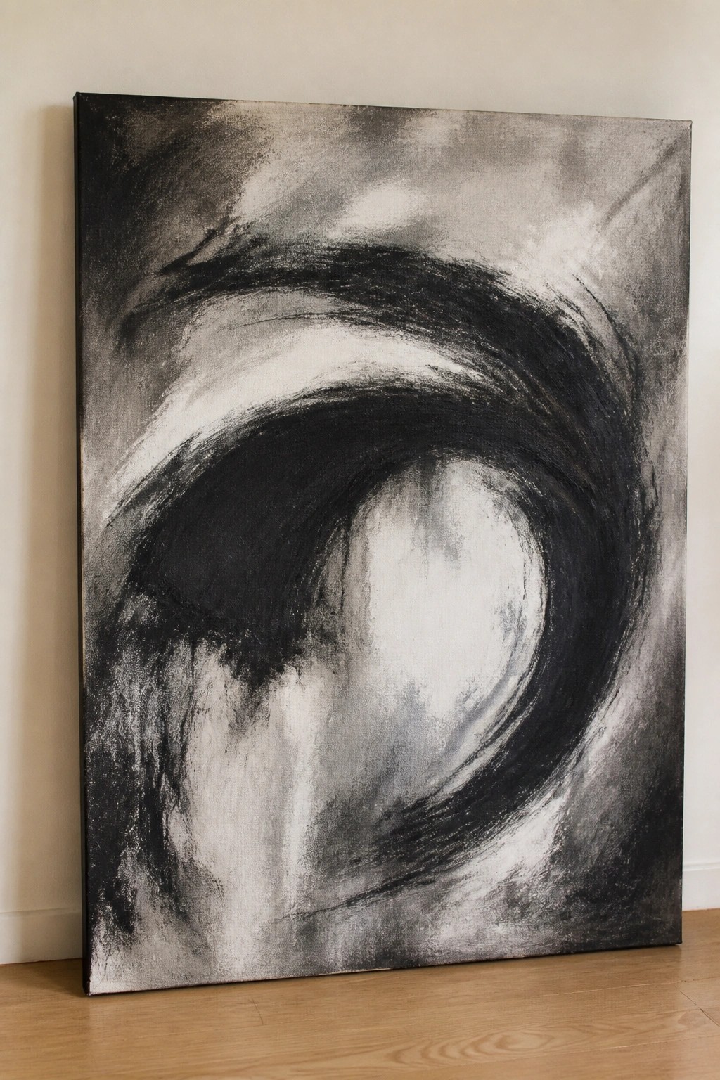 Large abstract black-and-white swirling vortex painting leaning on wooden floor against wall