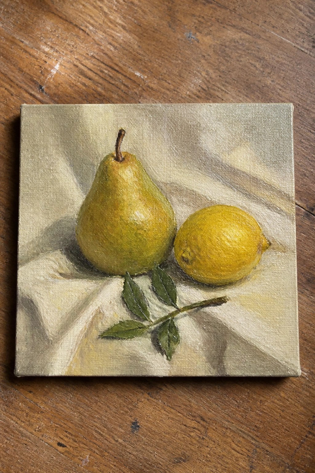 Yellow-green pear and lemon with leaves on draped fabric in still life painting
