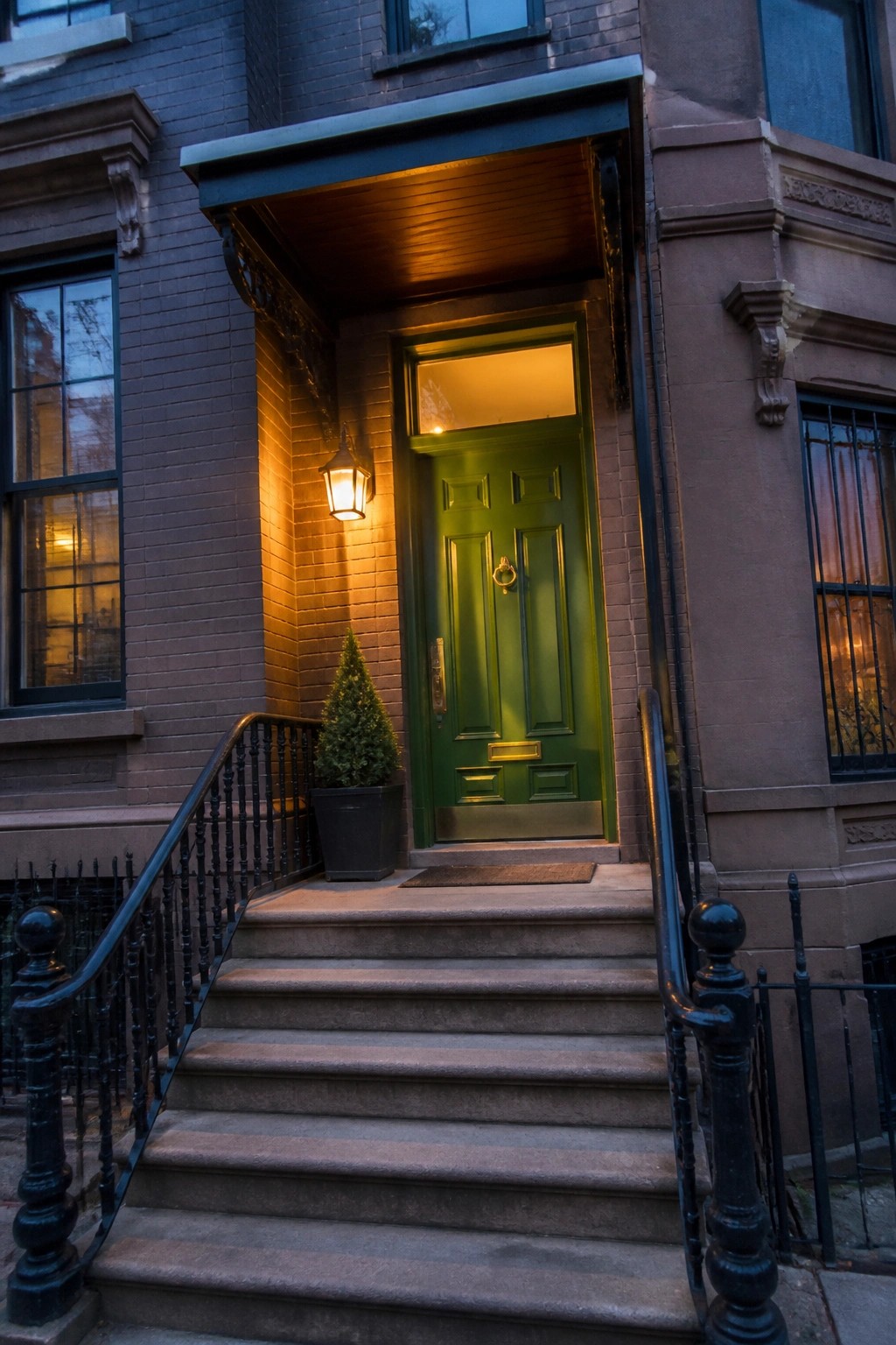 A deep green front door on a brick house with stone steps and black railings.
