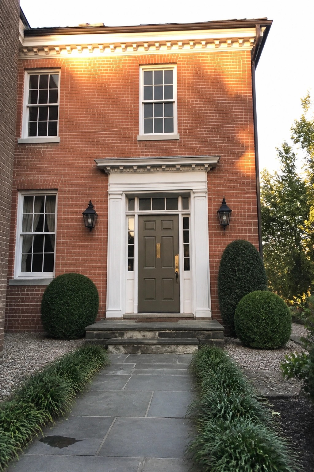 A muted olive green front door on a red brick house with white trim.