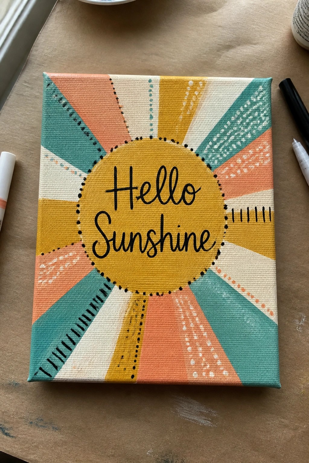 A square canvas with a sunburst design in teal, orange, yellow, and cream segments around a central yellow circle that reads