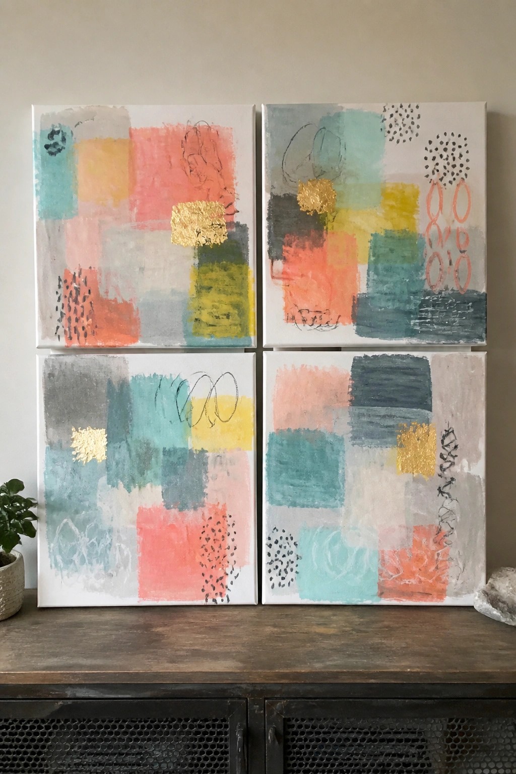 Four abstract paintings with coral, teal, yellow and gold accents on wooden cabinet