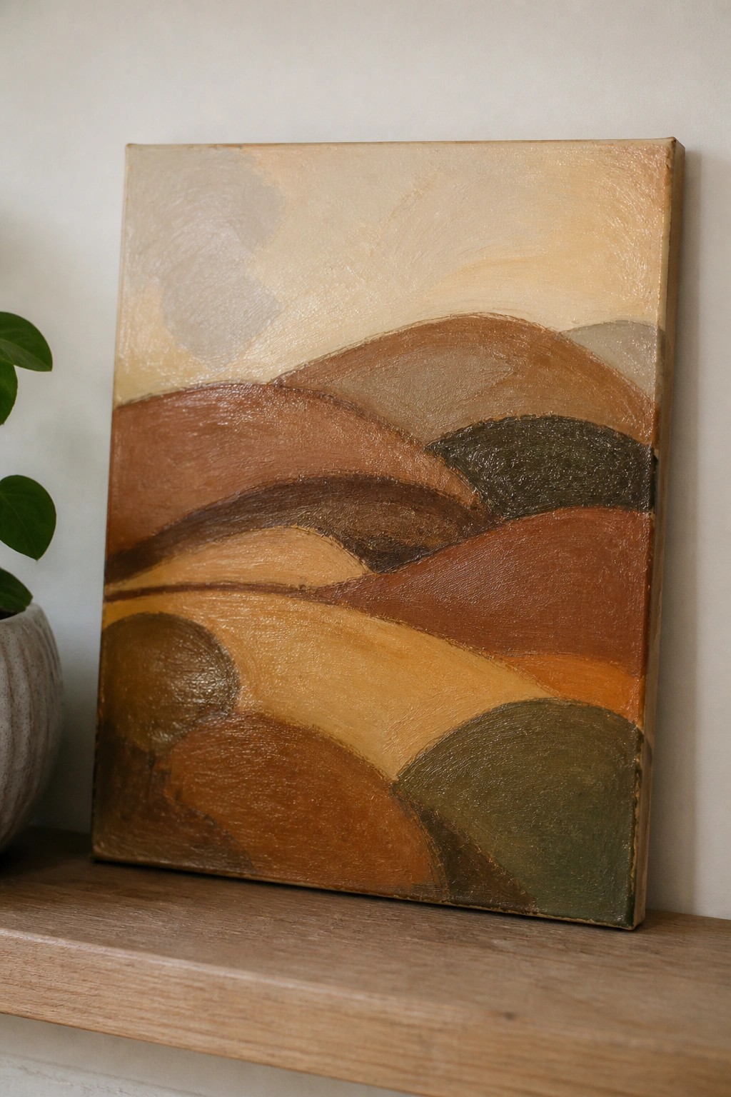 Abstract landscape painting with rolling hills in earthy browns and oranges on wooden shelf