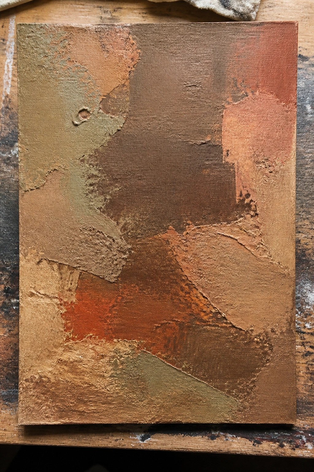 Textured abstract painting in earthy browns, oranges, and greens on wooden surface