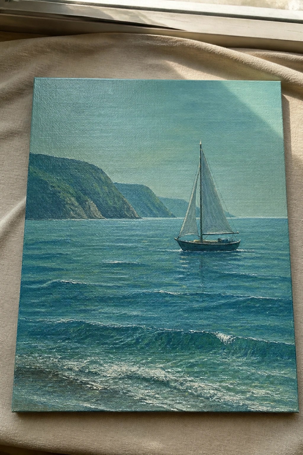 Square canvas painting of sailboat on wavy blue-green sea with green cliffs behind.