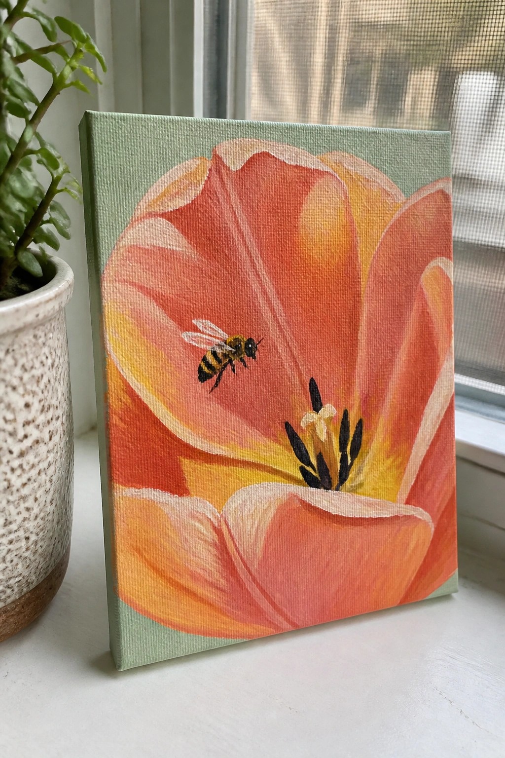 Orange tulip painting with bee on light green canvas beside potted plant.