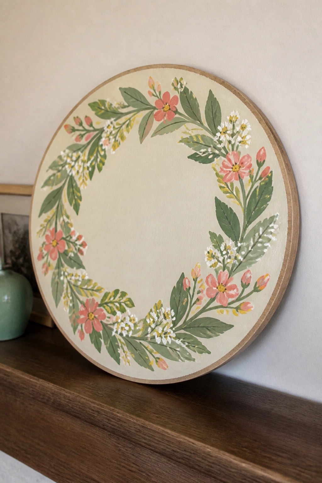 Round wooden plaque with pink floral wreath on beige background