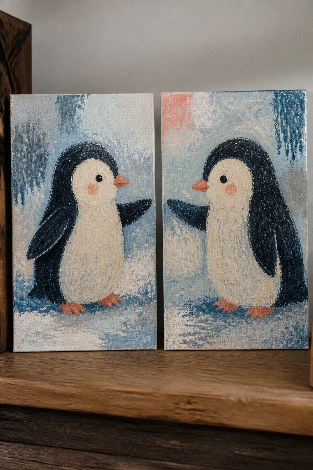 Two canvas paintings of penguins facing each other on a wooden shelf.