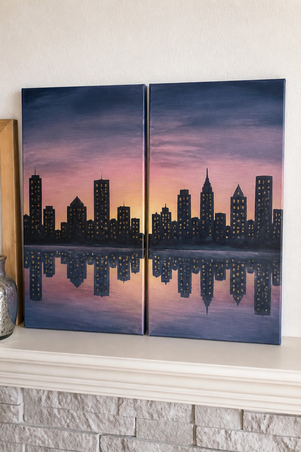 Two paintings of a city skyline silhouette with glowing windows reflected in water at sunset